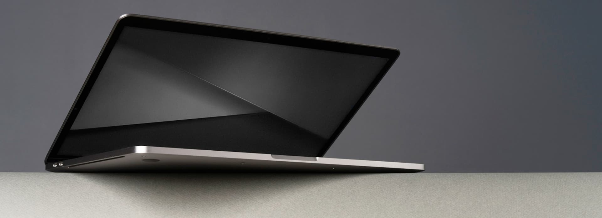 A sleek laptop partially open, displayed against a minimalist gray background, showcasing its slim design and reflective screen.