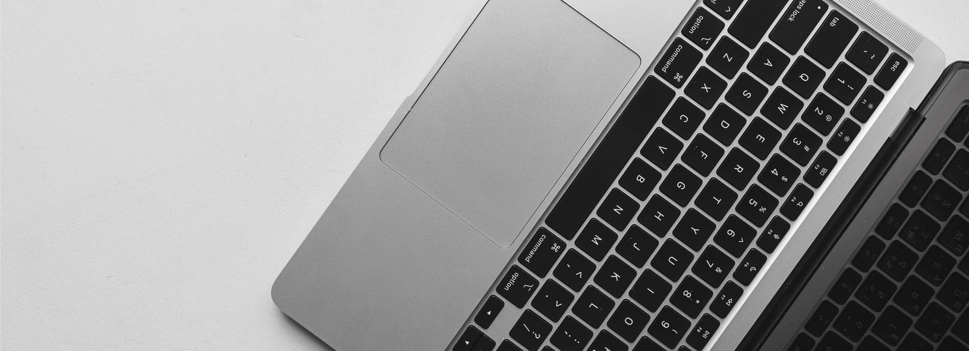 Aerial view of an open laptop with a black keyboard and silver casing on a white surface, showing the touchpad and partial keyboard.
