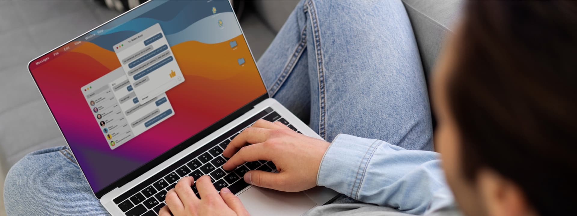 Person using a laptop on a couch, with a colorful desktop wallpaper and messaging app window open on the screen.