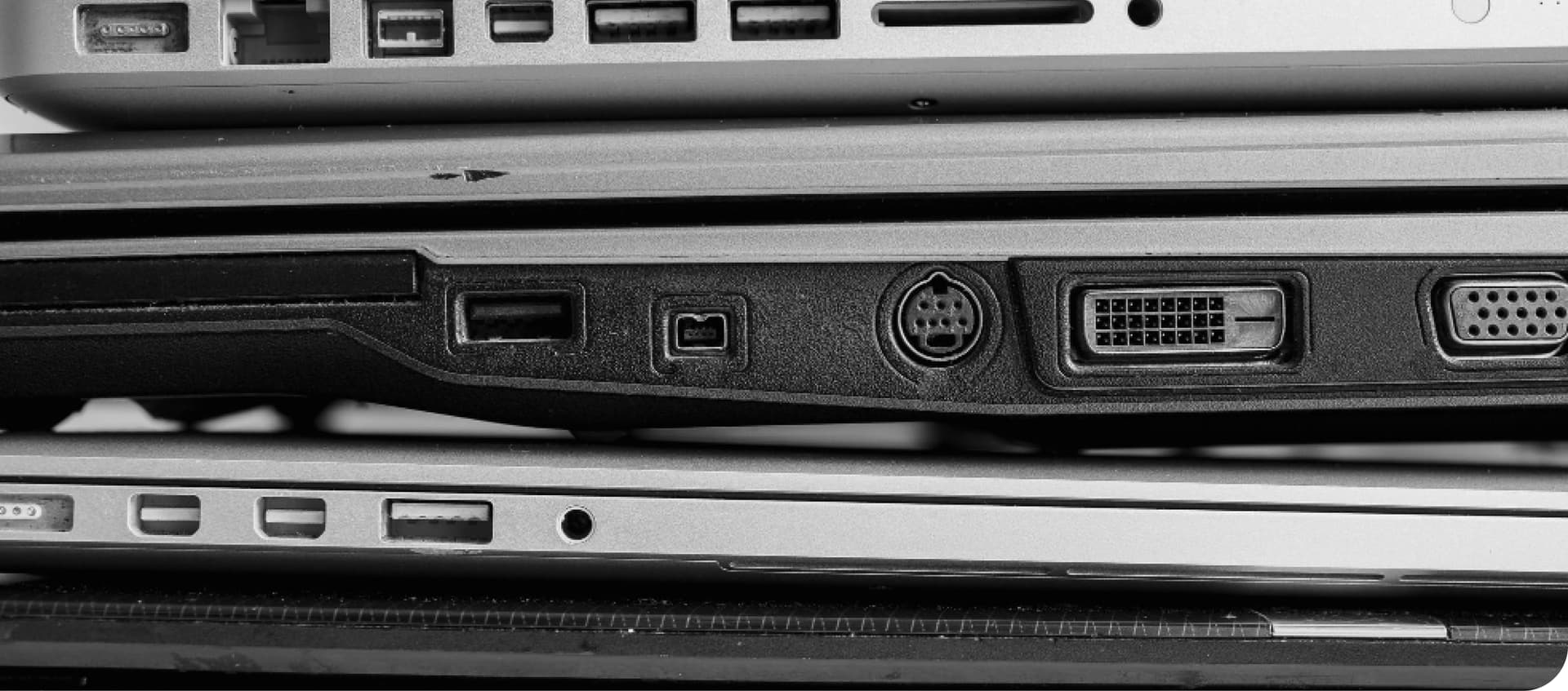 Stacked laptops showing various ports, including USB, DVI, and audio, in a black and white close-up view.