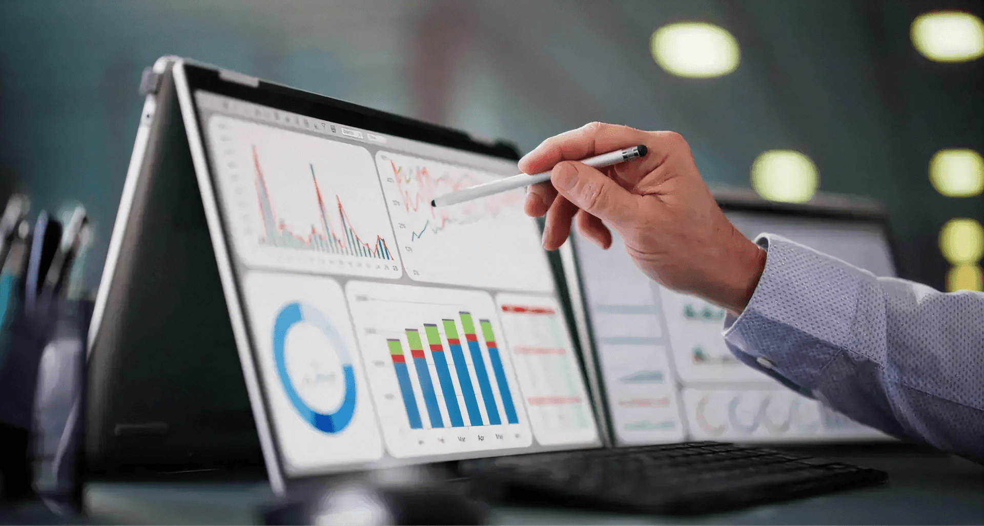 A person using a stylus to point at graphs and charts displayed on a foldable laptop screen, showing financial data and analytics.