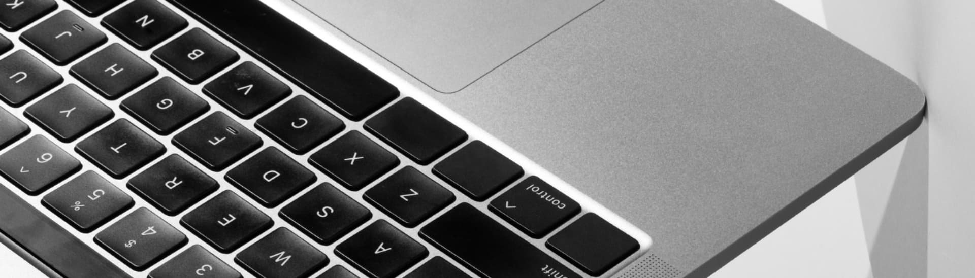 Close-up of a sleek laptop keyboard and touchpad, showcasing the corner of the device in a minimalist design with silver and black keys.