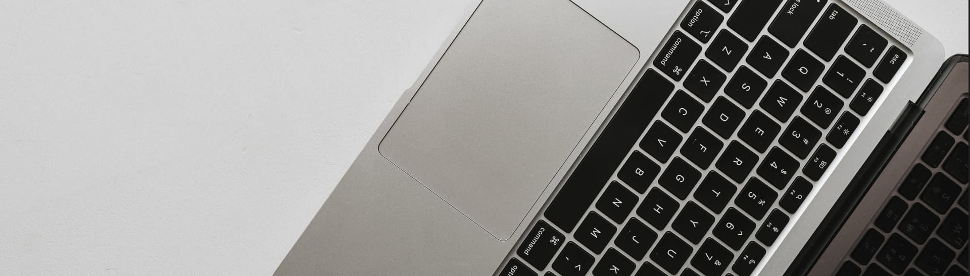 Close-up of a laptop keyboard and touchpad on a white surface, viewed from above, showing the black keys and silver body.
